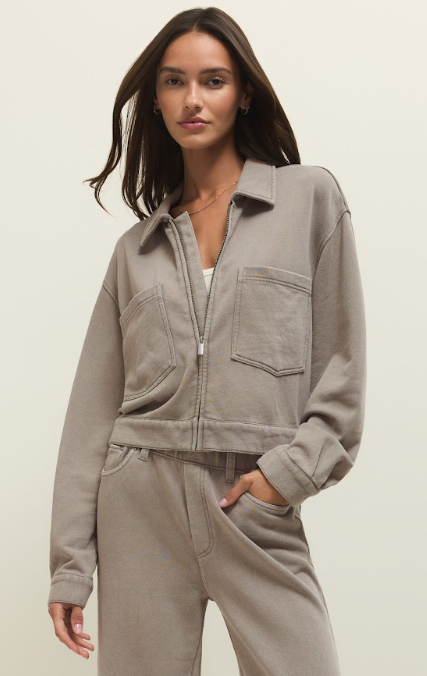 Woman wearing a beige zip-up hoodie and pants on a plain background